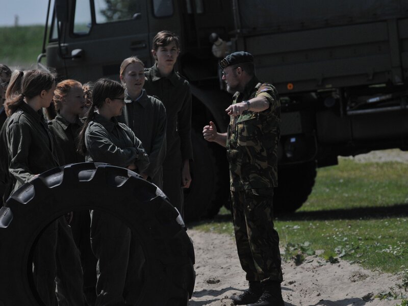 Militair geeft, voor een vrachtwagen, uitleg aan leden van het Young Fire & Rescue Team 